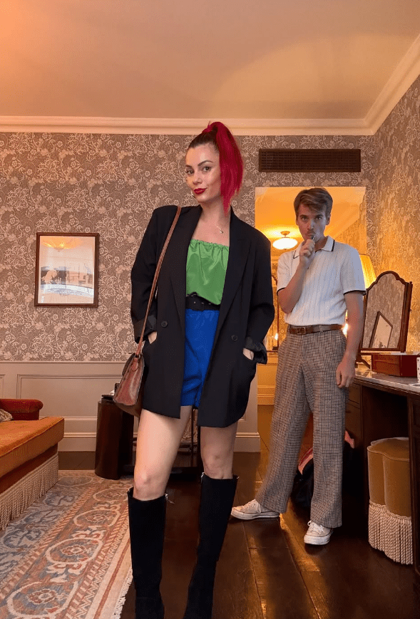 Photo of a woman in a black blazer, green top, and blue shorts, and a man in a white shirt and plaid pants.