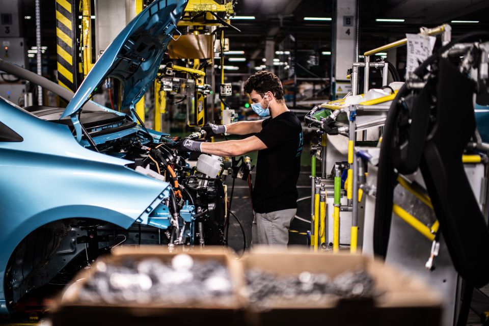 Worker wearing a mask assembling a car on an assembly line.