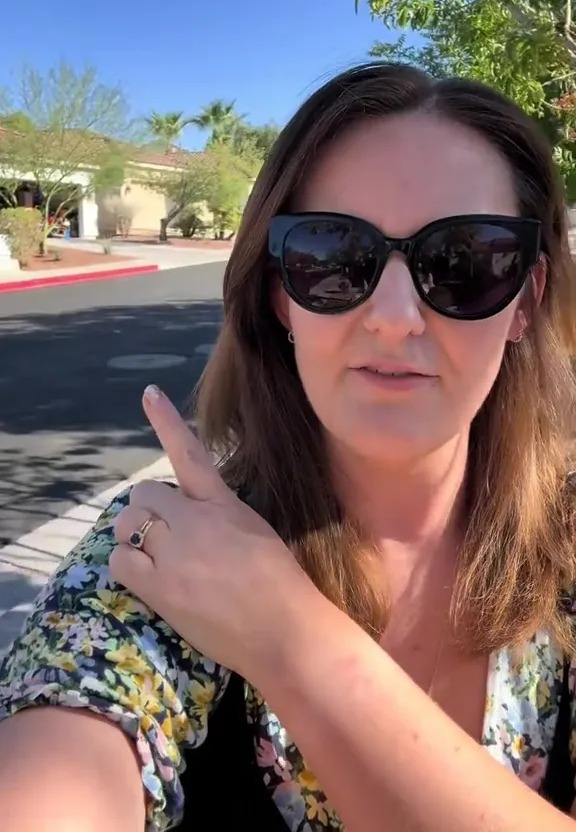 Woman in sunglasses points to houses on a sunny street.