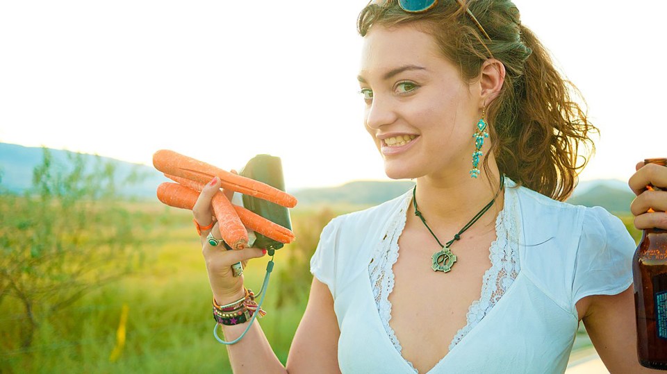 Woman at a festival holding carrots and a beer.