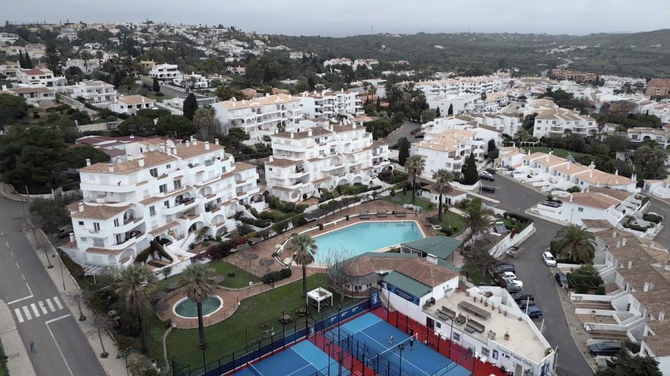 Aerial view of Ocean Club complex in Praia da Luz with buildings, swimming pools, tennis courts, and surrounding landscape.