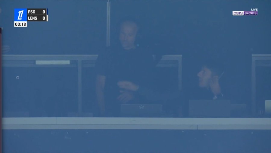 Two sports commentators behind glass at a match between PSG and LENS.