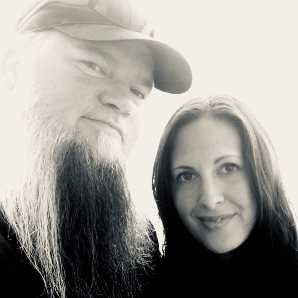 Black and white photo of a man with a long beard and a woman, who is the man's wife, smiling.