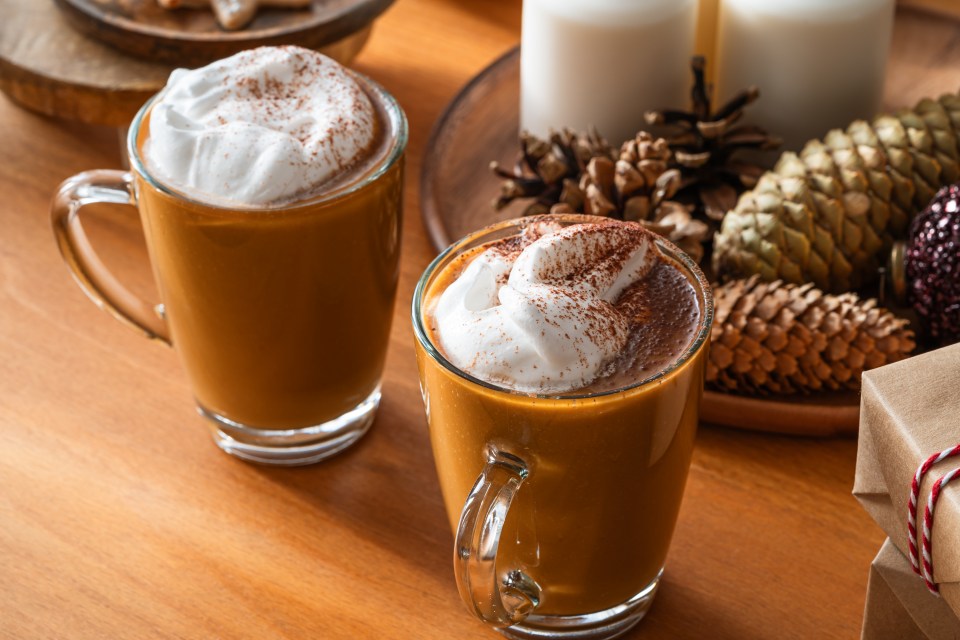 Two mugs of pumpkin spice latte with whipped cream and cinnamon on a wooden table with Christmas decorations.