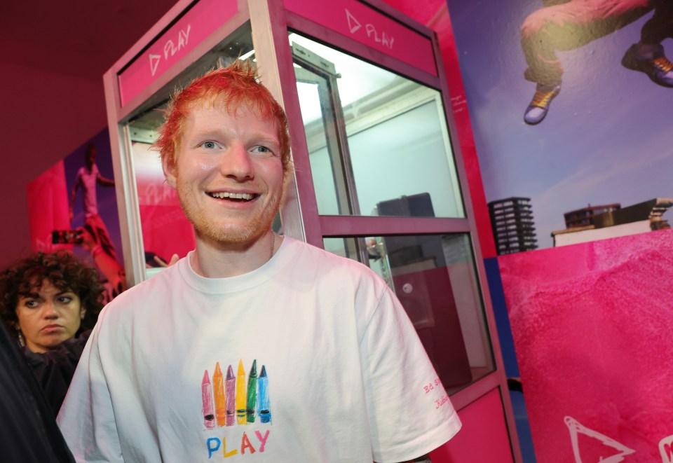 Ed Sheeran attends the KidSuper x Ed Sheeran event in a white t-shirt with crayons and the word "PLAY" on it.