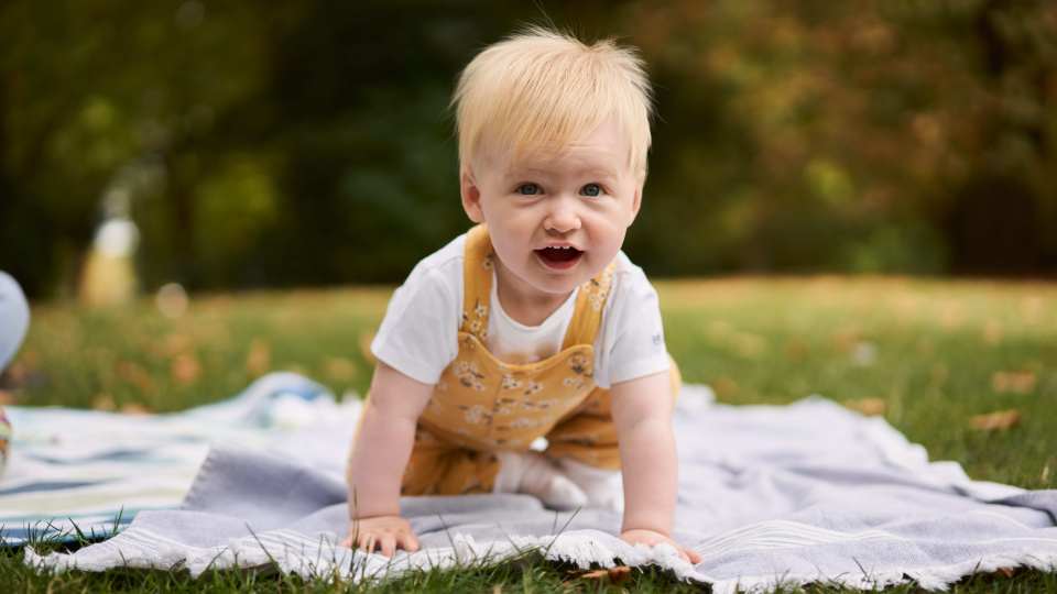 Rosie Bridge, an infant with Batten disease CLN2, smiling while crawling on a blanket outdoors.