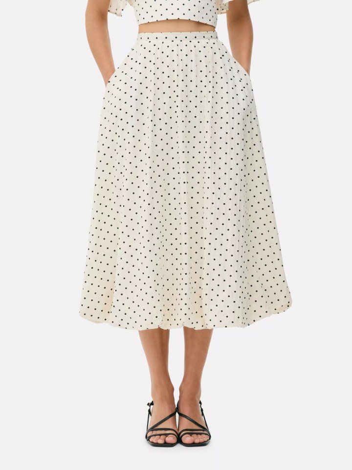 A person wearing a white polka dot midi skirt with pockets and black strappy heels.