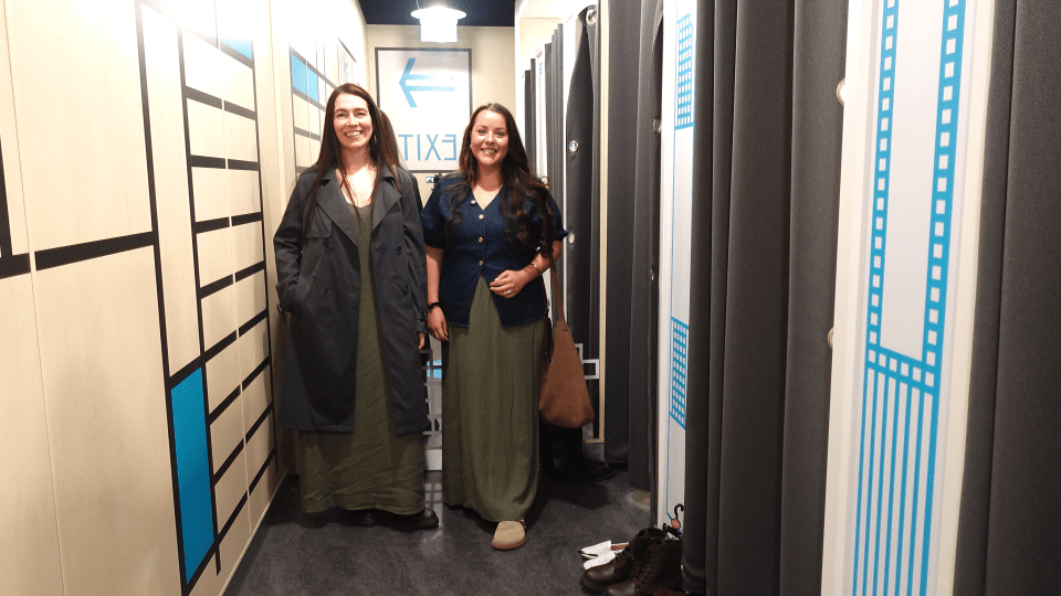Two women smiling in a narrow hallway with an "EXIT" sign.