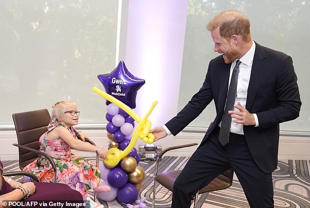 Prince Harry play-fights using balloon swords with nine-year-old Gwen Foster, a WellChild Award recipient
