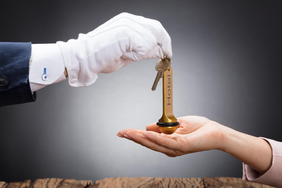 A gloved hand gives a hotel key to another hand.