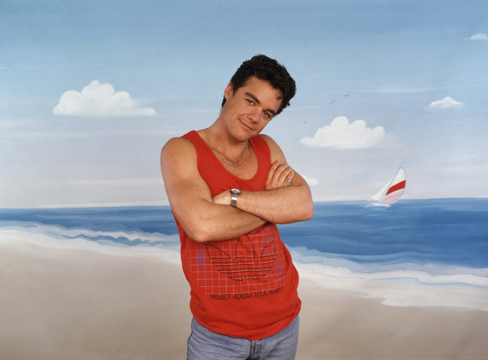 Stefan Dennis, best known for his role in 'Neighbours,' posing in front of a painted seaside backdrop.