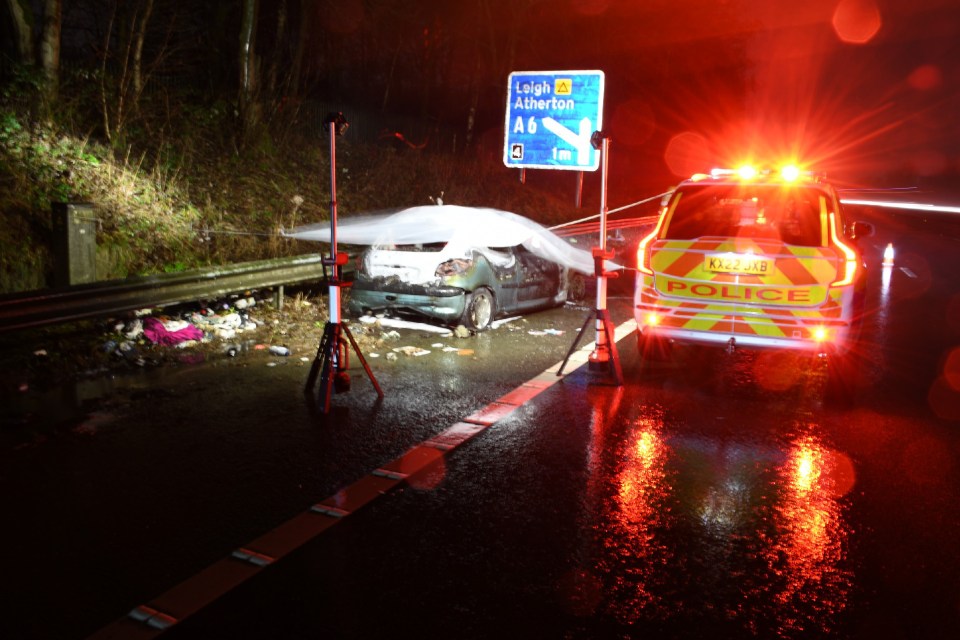 Burnt-out car on highway at night, police car present.
