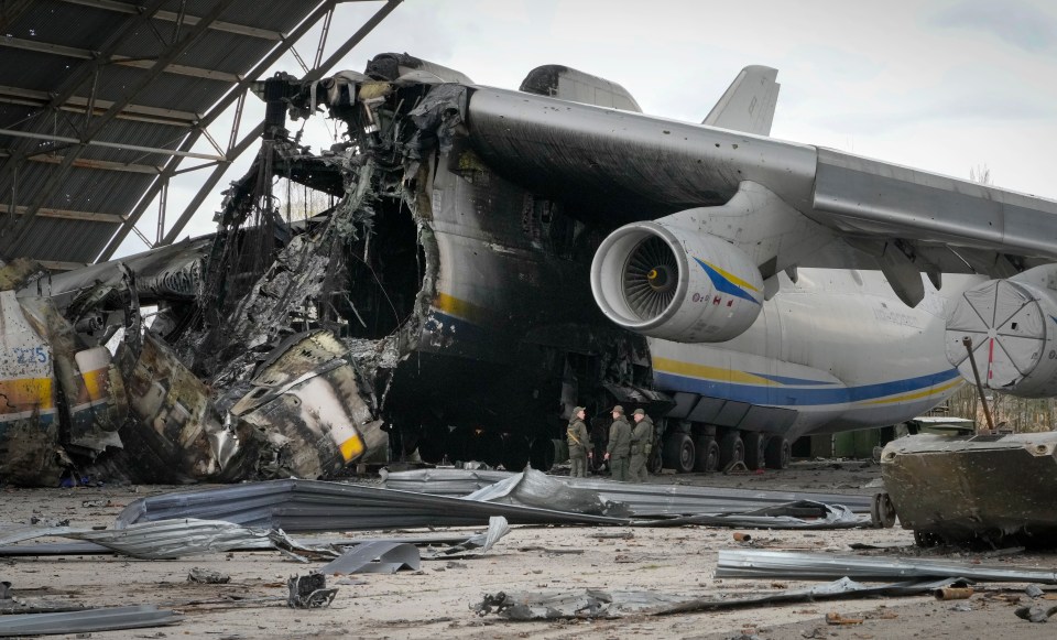 Three Ukrainian soldiers stand by the remains of the destroyed Antonov An-225 cargo aircraft in a hangar.