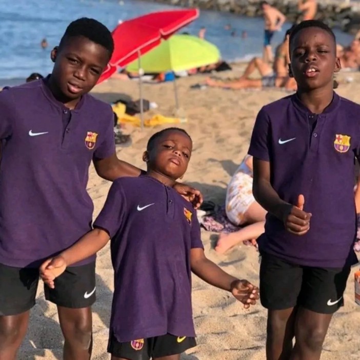 Three boys wearing purple Barcelona FC shirts and black shorts on a beach.