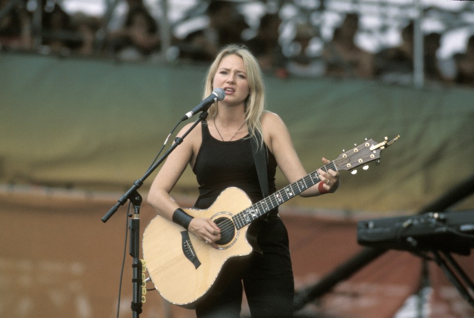 Jewel performing on stage with an acoustic guitar.