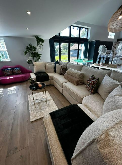 Katie Price's living room with a large L-shaped cream sofa, a pink lip-shaped sofa, and wooden floors.