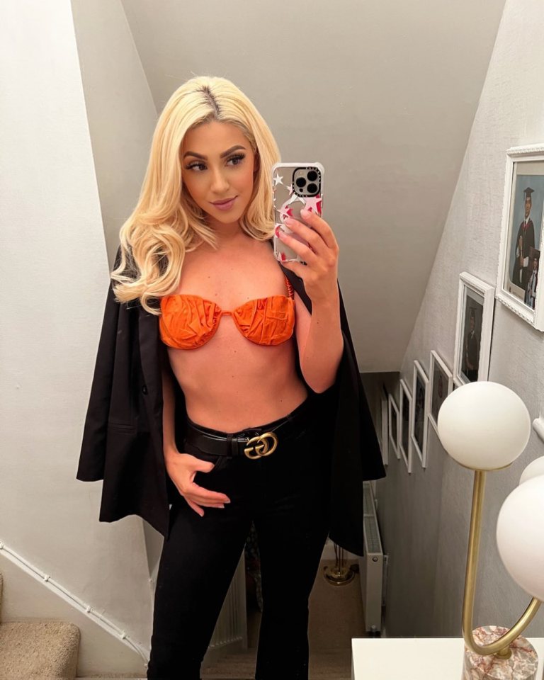 Bianca Petronzi taking a mirror selfie wearing an orange top, black blazer, and black pants with a Gucci belt.