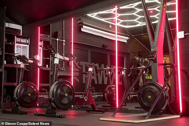 The gym is decorated in bright pink neon lights and features a range of state of the art equipment including exercise bikes, squat racks and free weights