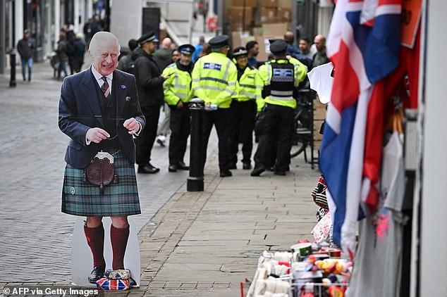 Police walk past a cardboard cutout featuring an image of King Charles III in Windsor today