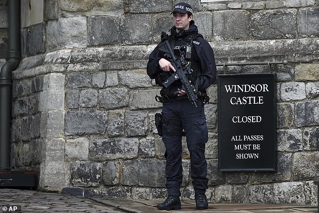 An armed police officer holds his weapon as he stands guard outside Windsor Castle today