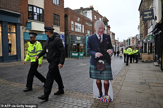 Police walk past a cardboard cutout featuring an image of King Charles III in Windsor today