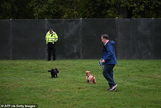 A man walks dogs as a police officer stands guard by a fence blocking off the Long Walk today
