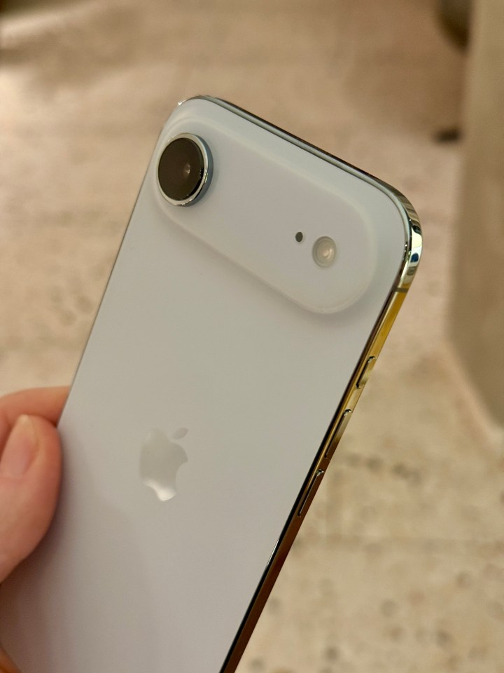 Close-up of a hand holding a white iPhone with a large camera lens and Apple logo.