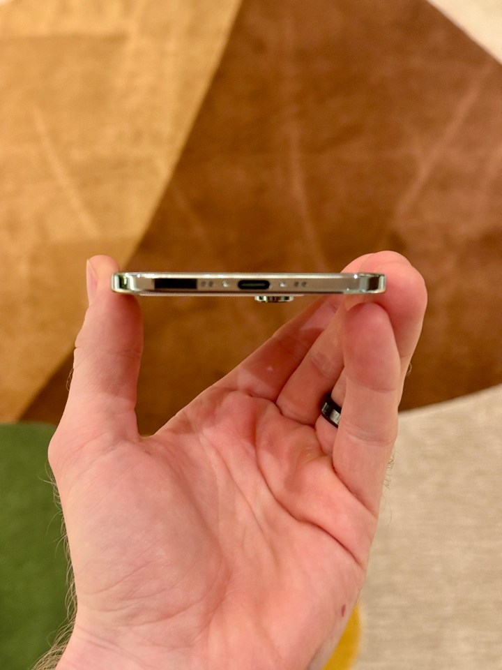 A hand holding an iPhone with a USB-C charging port on the bottom.