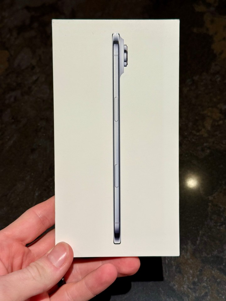 Hand holding a white iPhone box displaying the phone's side profile.
