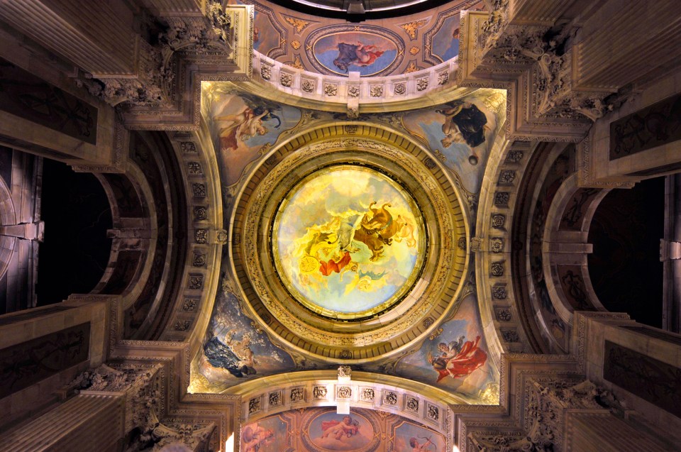 The ornate ceiling of the Great Hall at Castle Howard in Yorkshire, UK, featuring a large circular painted mural of mythological figures surrounded by intricate architectural details and smaller painted panels.