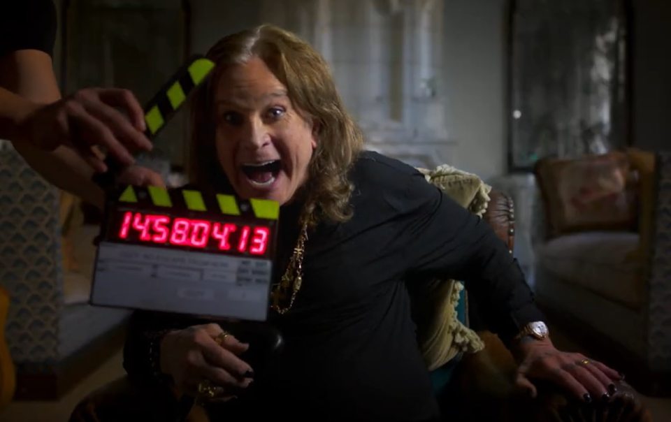 Ozzy Osbourne looking excited, leaning back in a chair, with a clapperboard in front of him.
