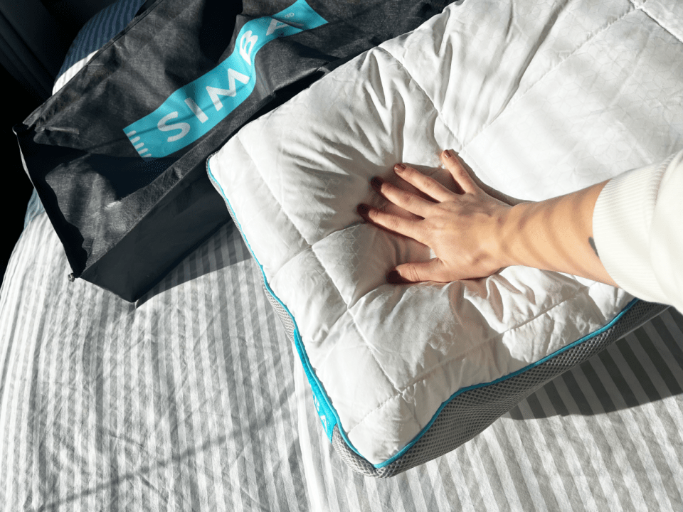 A person's hand pressing on a Simba pillow next to a Simba branded bag.
