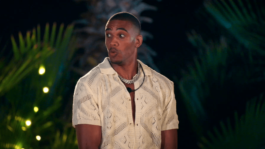 Man with a surprised expression, wearing a cream knit shirt and a thick silver chain.