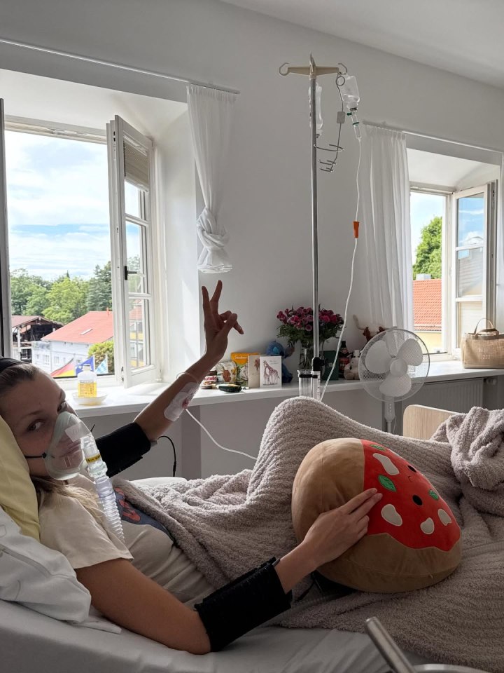Bella Hadid in a hospital bed with an oxygen mask, giving the peace sign.