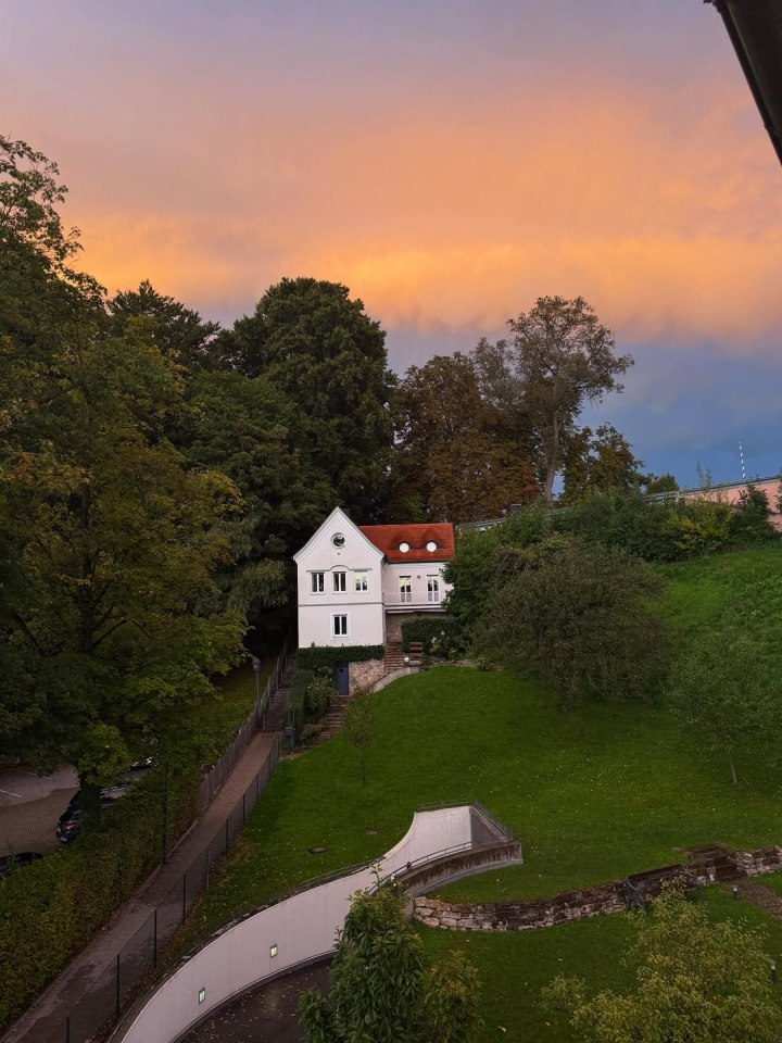 White house with a red roof on a hill with a colorful sunset sky.