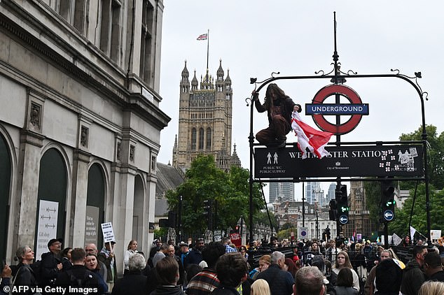 A protester unties a St George's cross flag from the Westminster Station underground sign near Parliament Square in London on September 17, 2025 during a national march organised by the Stop Trump Coalition against the State Visit of US President Donald Trump. US President Donald Trump arrived in Britain for an unprecedented second State Visit, with the UK government rolling out a royal red carpet welcome to win over the mercurial leader. (Photo by JUSTIN TALLIS / AFP) (Photo by JUSTIN TALLIS/AFP via Getty Images)