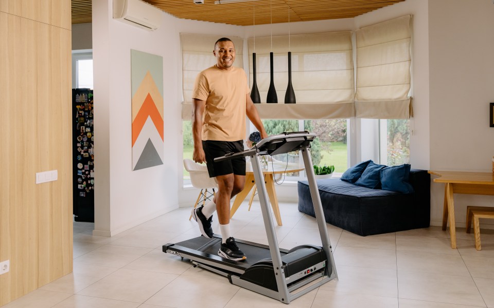Man in a light orange shirt and black shorts walking on a treadmill in a bright room.