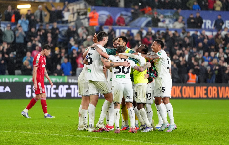 Swansea City players celebrate a victory during the Carabao Cup third round match, while an opposing player in red walks away dejectedly.