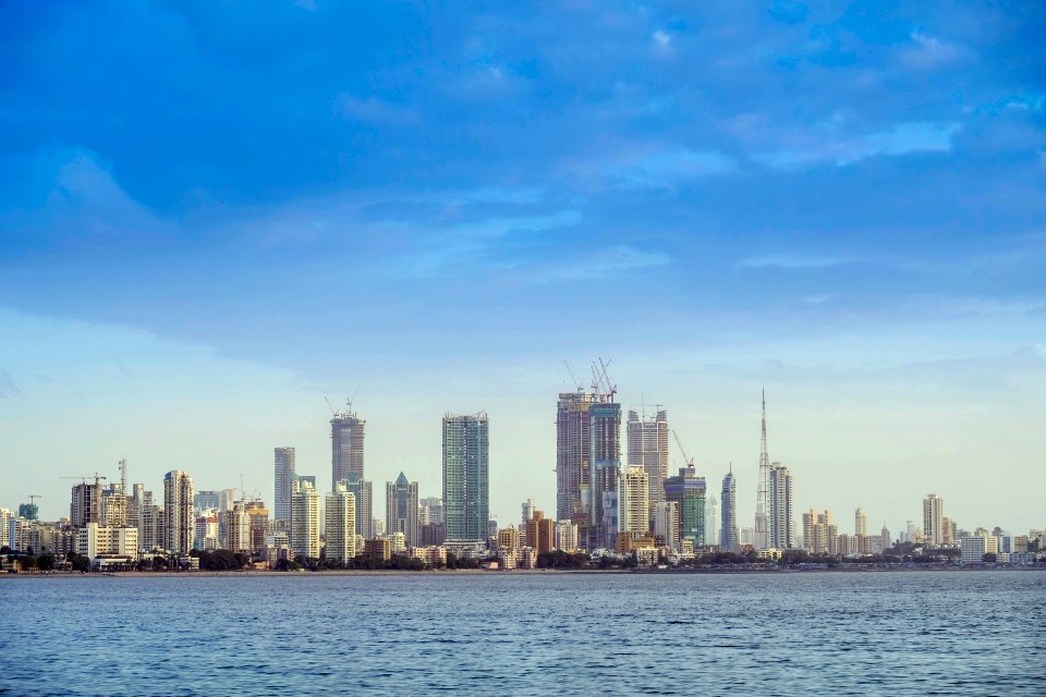 Urban skyline of Mumbai city with tall buildings and cranes from the Arabian Sea.
