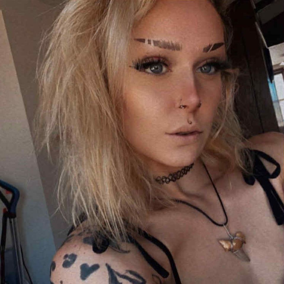 Savanah White with blonde hair and nose piercings, wearing a choker and shark tooth necklace.