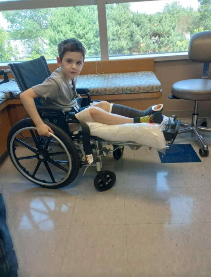 Malakye White, aged 8, sits in a hospital wheelchair with a cast on his left leg.