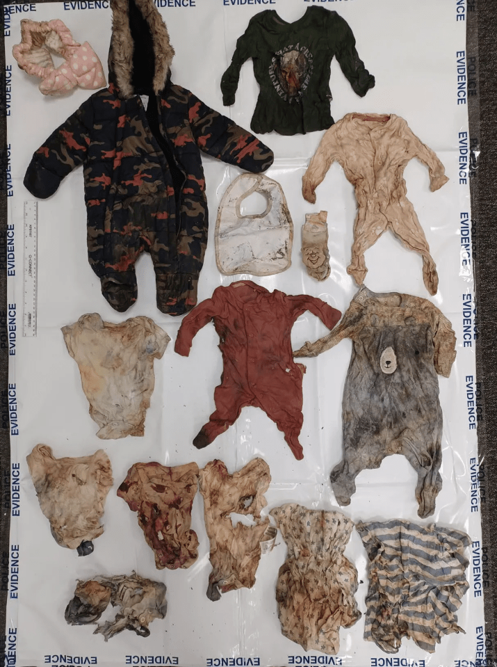Infant clothing and accessories, including a camouflage snowsuit, bib, and several onesies, some stained or dirty, laid out on a white surface with "EVIDENCE" tape.