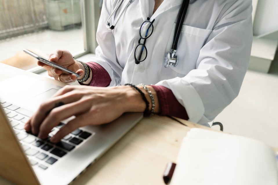 A female doctor using a laptop and smartphone.