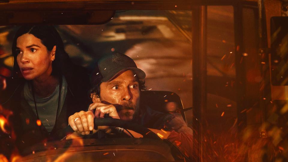Matthew McConaughey and America Ferrera in a bus surrounded by fire, looking scared.