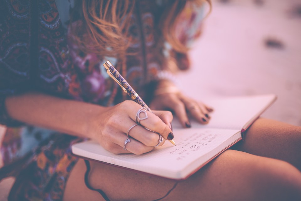A boho woman wearing a floral dress writing in her diary.