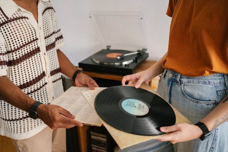 Two people holding vinyl records and sleeves, with a turntable in the background.