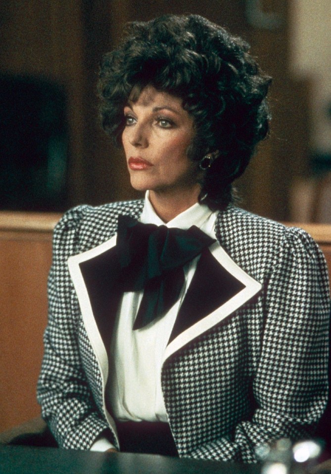 Joan Collins in a houndstooth jacket with a white collar and black bow, wearing heavy makeup and dark, curly hair.