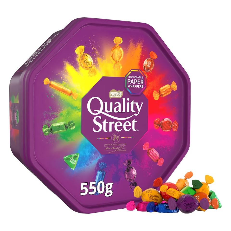 A purple, octagonal tin of Quality Street chocolates with assorted wrapped chocolates spilling out.