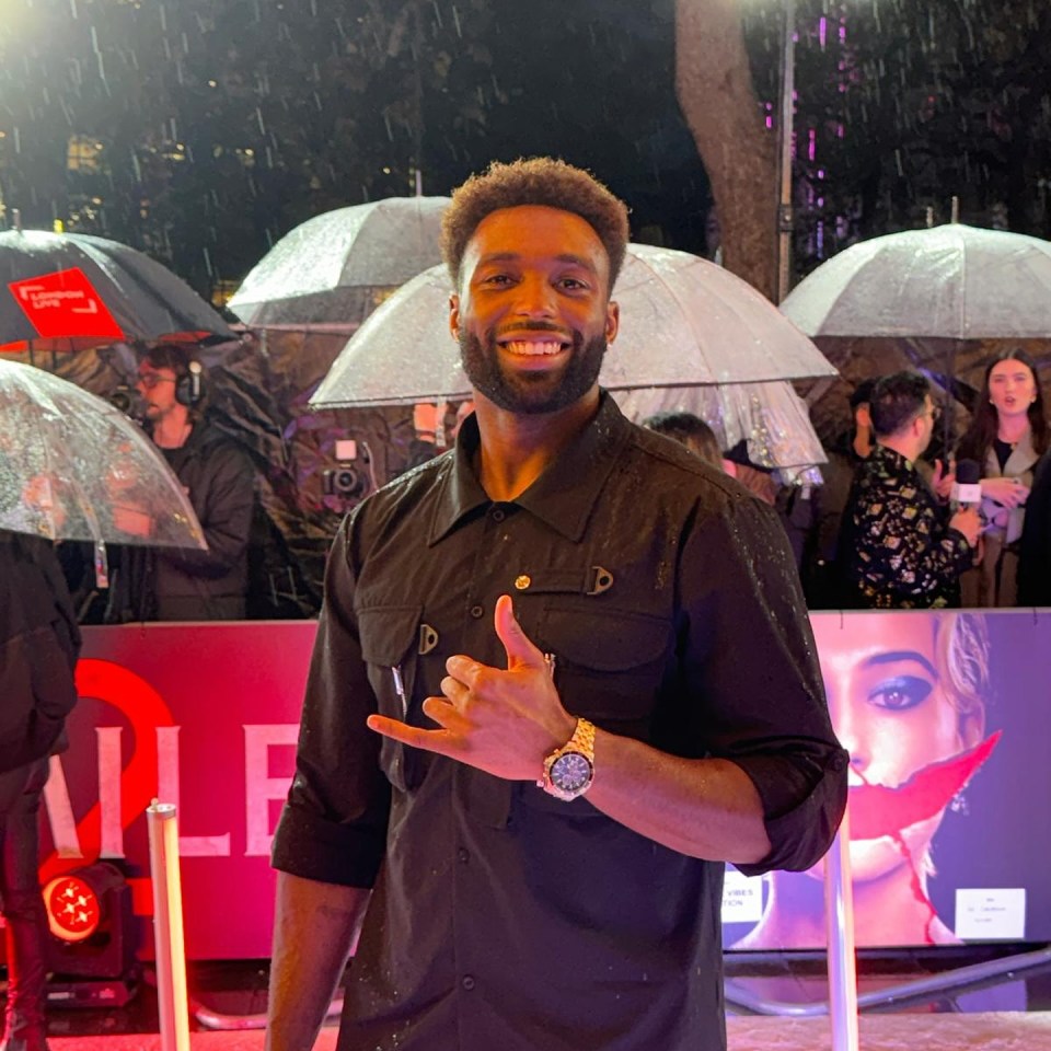Married at First Sight's Paul Liba smiling and giving a shaka sign on a rainy red carpet event.