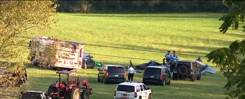First responders at the scene of a plane crash in a grassy field.